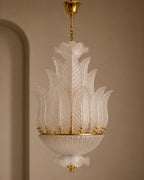 An elegant Italian Murano-style glass chandelier with intricate white textured glass leaves and gold brass hardware, suspended against a warm beige wall.