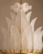 A close-up of a decorative chandelier featuring multiple translucent textured glass leaf-like shades arranged in a tiered circular structure, with gold-toned metal hardware and hanging chain visible at the top.