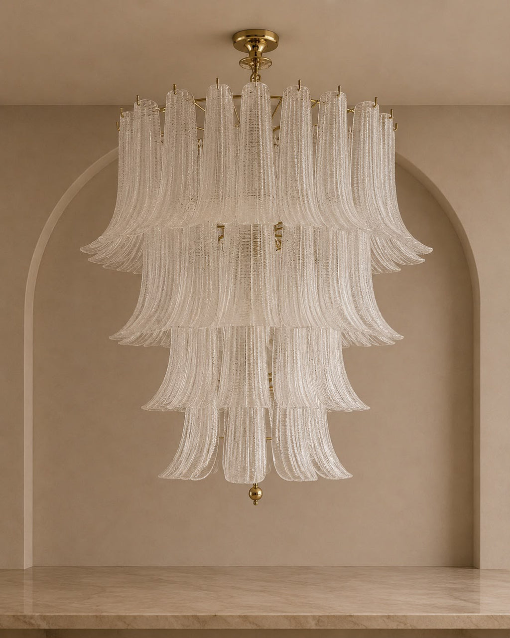A tiered chandelier with cascading textured glass shades and gold-toned hardware, suspended in front of a beige arched wall.