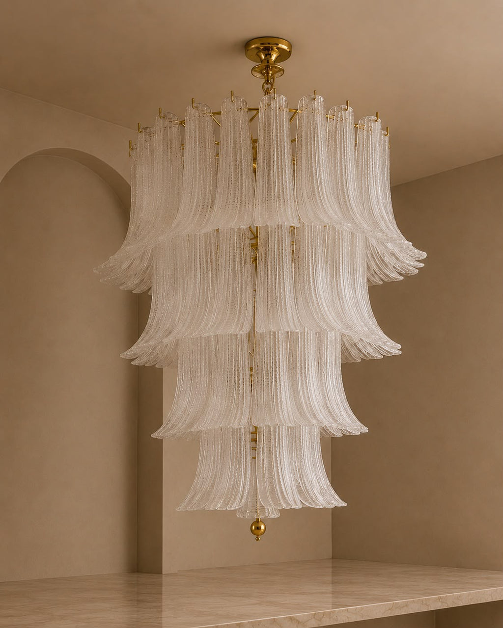 A tiered chandelier with cascading translucent white glass fluted rings and gold-toned metal hardware, hanging in a warm beige interior room.