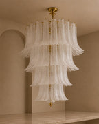 A tiered chandelier with cascading translucent white glass fluted rings and gold-toned metal hardware, hanging in a warm beige interior room.