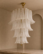 A large tiered chandelier with cascading translucent white glass shades and gold-toned metal hardware, hanging in a warm beige interior room.