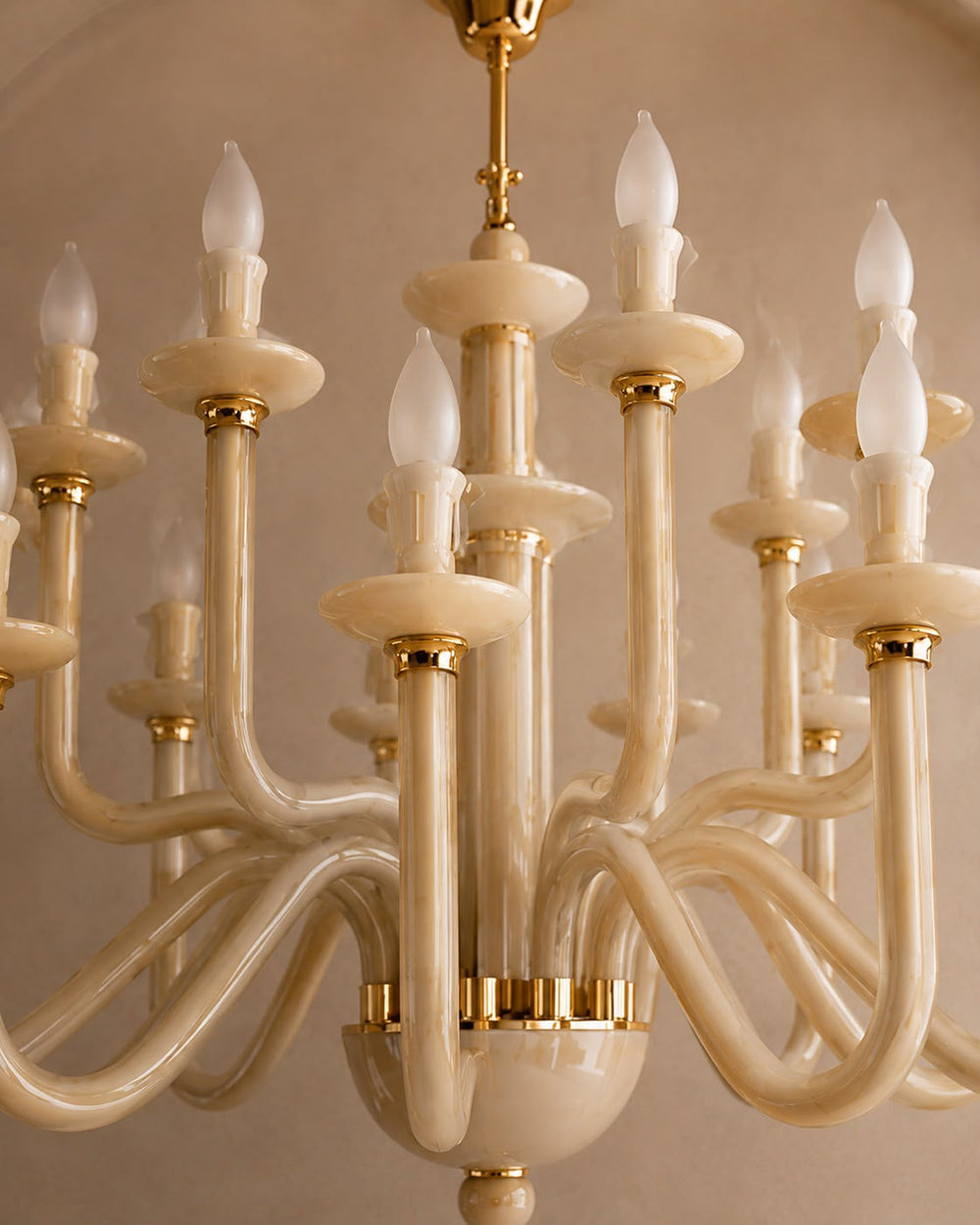 A close-up of a multi-arm chandelier with curved cream-colored arms and gold metal accents, shown against a warm beige background.
