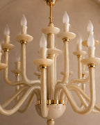 A close-up of a multi-arm chandelier with curved cream-colored arms and gold metal accents, shown against a warm beige background.