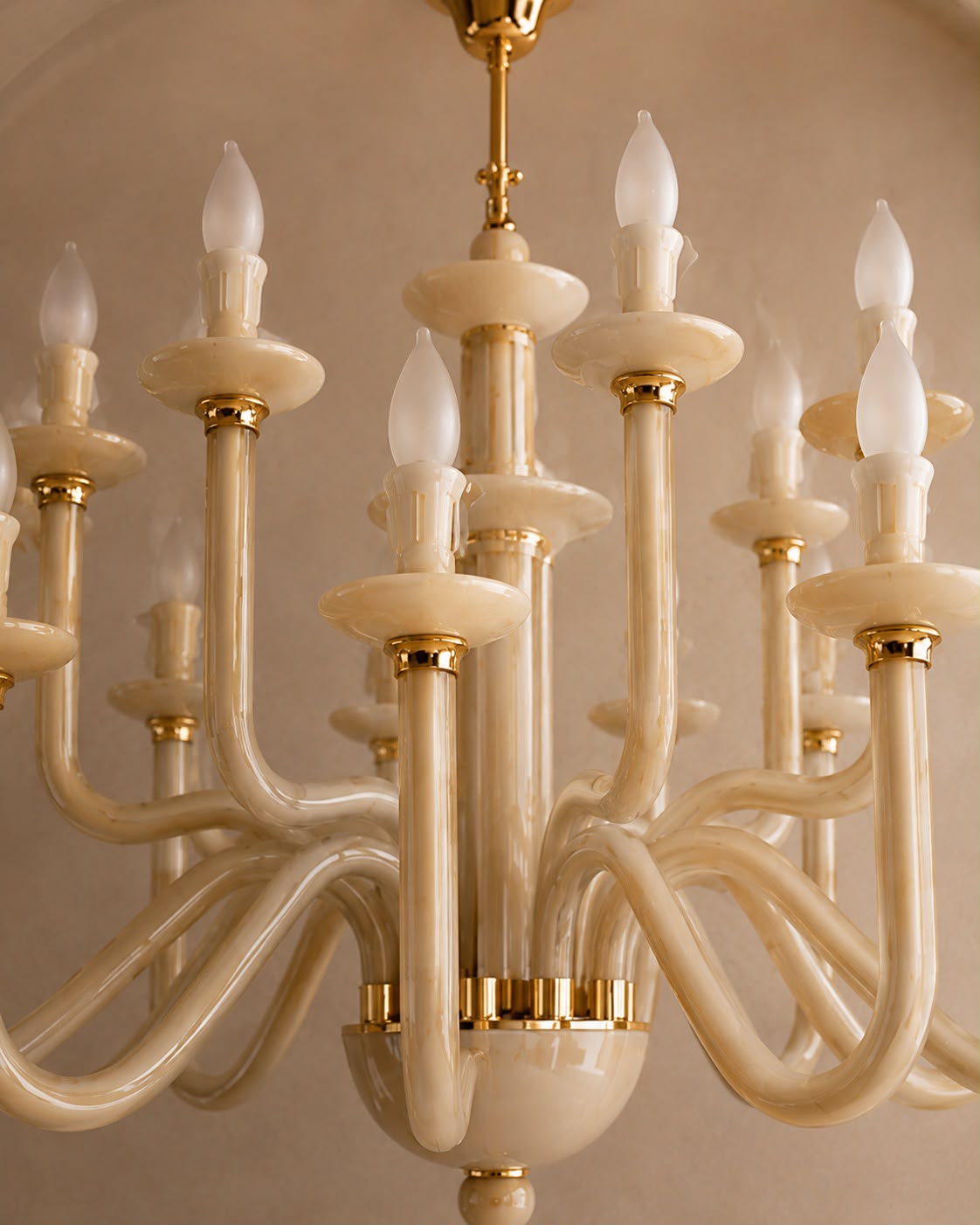 A close-up of a multi-arm chandelier with curved cream-colored arms and gold metal accents, shown against a warm beige background.