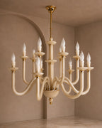 A multi-arm chandelier with curved cream-colored arms and polished gold-toned hardware, suspended in a warm beige room with arched walls.