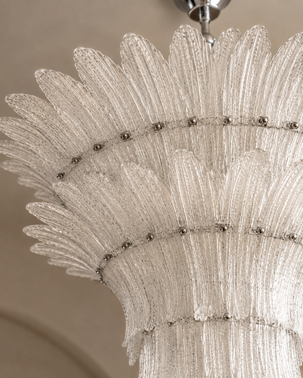 A close-up detail of a modern chandelier featuring textured, petal-like clear glass rods arranged in concentric rings with small metallic accents.