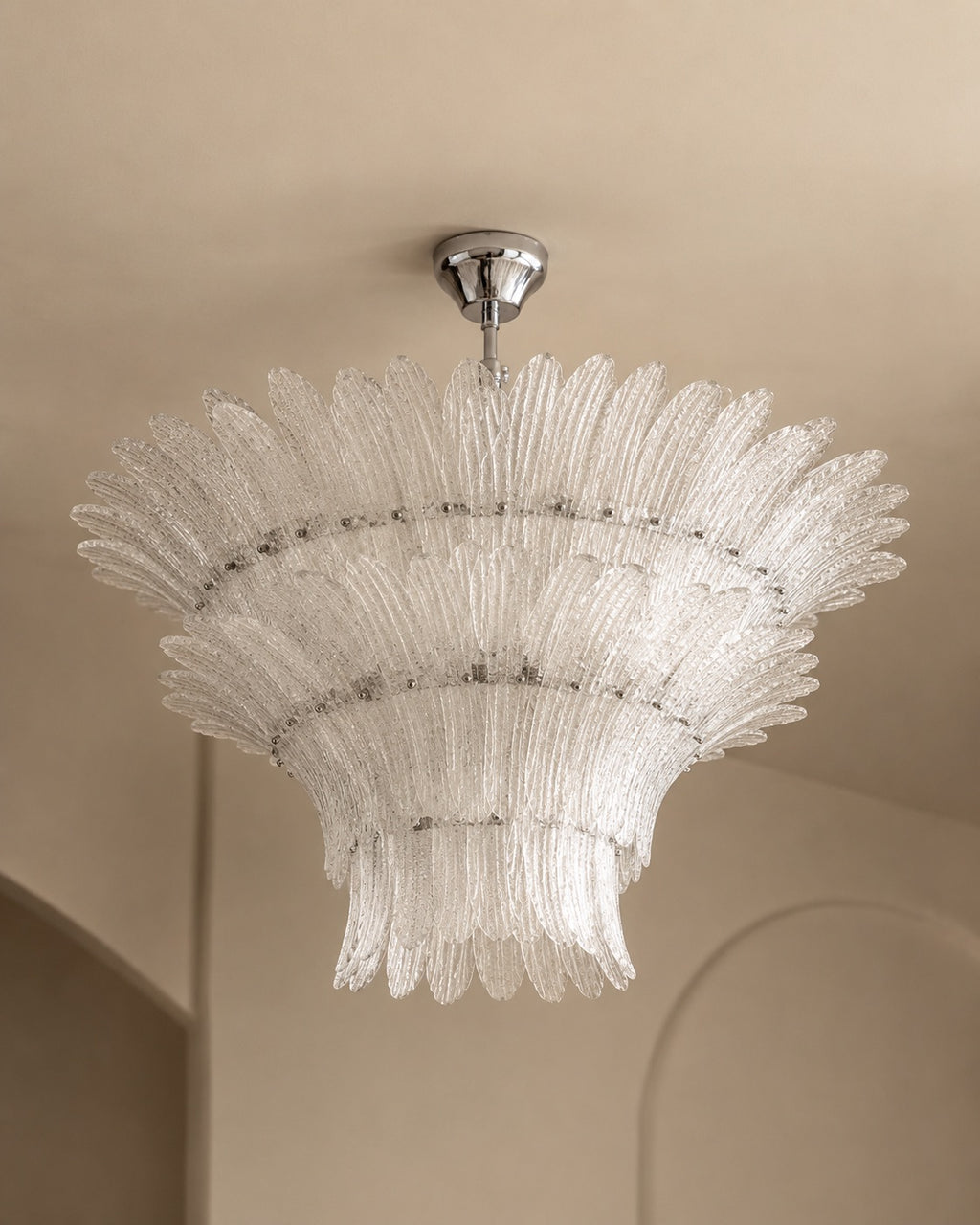 A tiered, fan-shaped clear glass chandelier with a polished silver ceiling canopy, suspended from a beige ceiling.