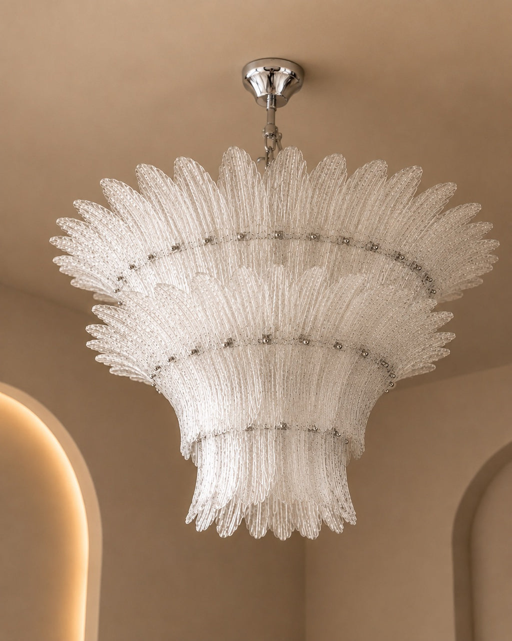 A tiered, sunburst-style chandelier with textured clear glass shades and a polished silver ceiling canopy, shown hanging in a warm beige interior.