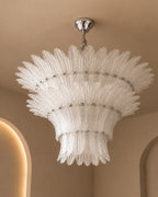 A tiered, sunburst-style chandelier with textured clear glass shades and a polished silver ceiling canopy, shown hanging in a warm beige interior.