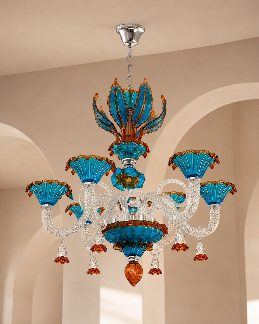An ornate chandelier with vibrant turquoise blue glass flower-shaped shades, clear crystal arms, and amber-orange accents, hanging from a silver ceiling canopy in a beige arched interior.