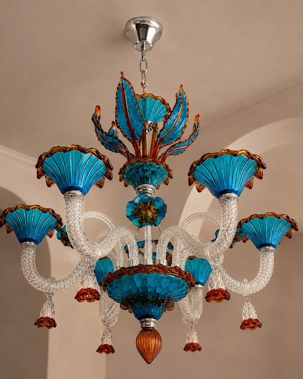 A decorative chandelier with six turquoise blue glass flower-like shades, clear textured glass arms, and amber-brown accents, hanging from a silver ceiling canopy in an indoor room.