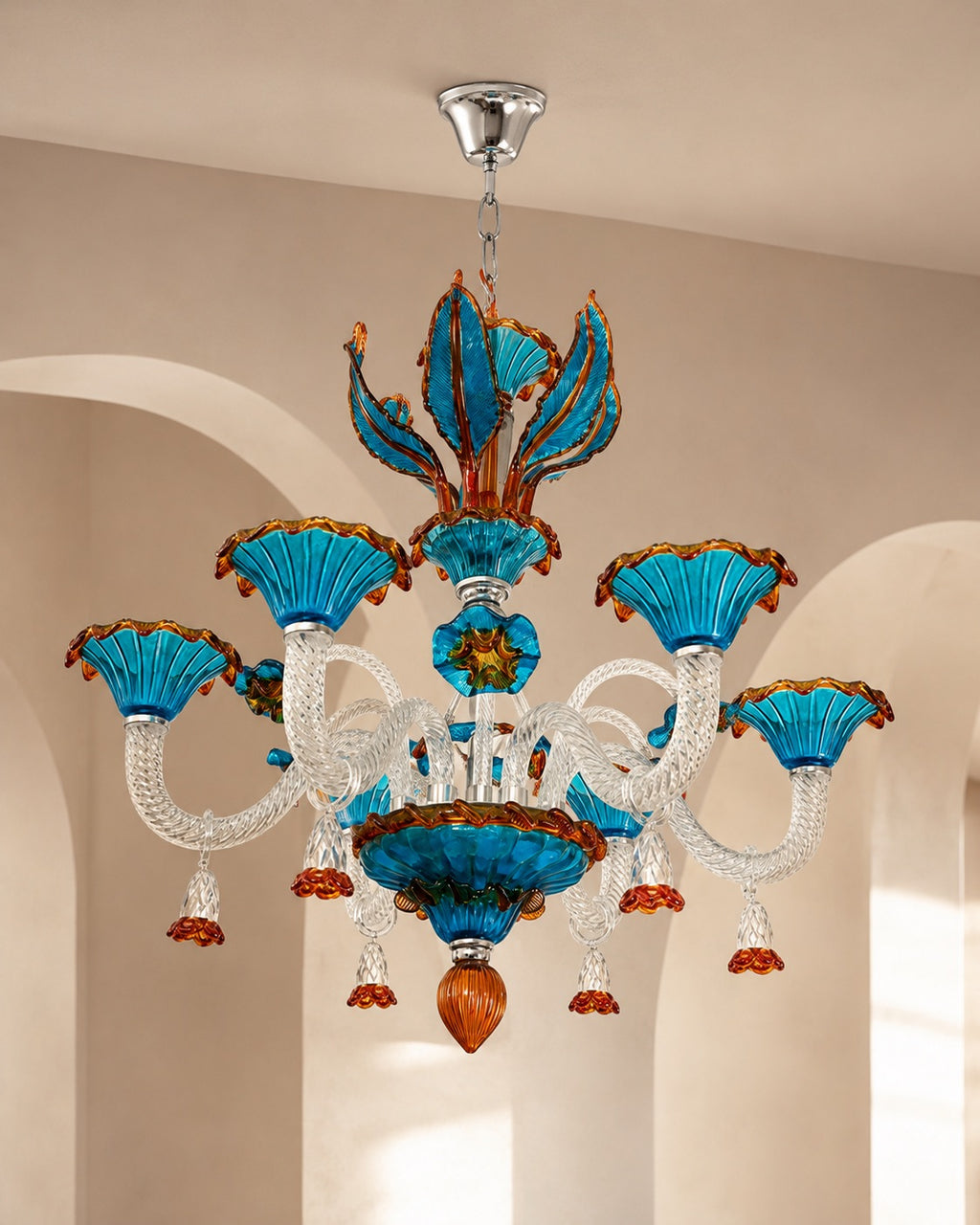 A decorative chandelier with turquoise blue glass shades, clear glass arms, and orange-brown accents, hanging from a silver ceiling canopy in an indoor room with beige walls and arches.
