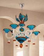 A decorative chandelier with turquoise blue glass shades, clear glass arms, and orange-brown accents, hanging from a silver ceiling canopy in an indoor room with beige walls and arches.