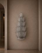 A tiered, lotus-shaped wall sconce with a textured silver mesh pattern, mounted on a warm beige plaster wall in an elegant interior hallway.