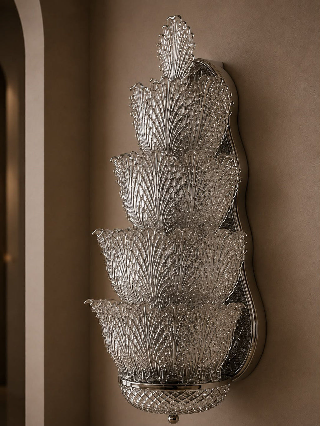 A tiered crystal wall sconce with five stacked textured glass bowls on a polished silver metal backing, mounted on a warm brown wall.