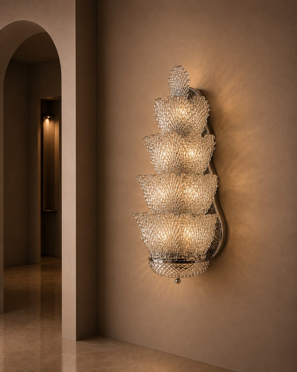 A tiered crystal chandelier wall sconce with multiple cascading crystal bowls emitting a warm golden glow, mounted on a beige plaster wall in an elegant interior hallway.