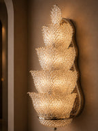 A tiered crystal wall sconce with a warm gold-toned metal frame, mounted on a beige wall.