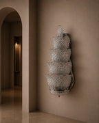 A sculptural, tiered wall sconce made of textured, clear glass or acrylic, mounted on a warm beige plaster wall in an elegant interior hallway.