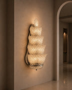 A modern wall sconce with five stacked, tiered crystal-like shades mounted on a beige plaster wall in an elegant interior hallway.