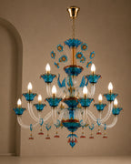A multi-tiered chandelier with blue glass flower petals, clear crystal arms, and gold-toned metal hardware, shown hanging against a beige wall.