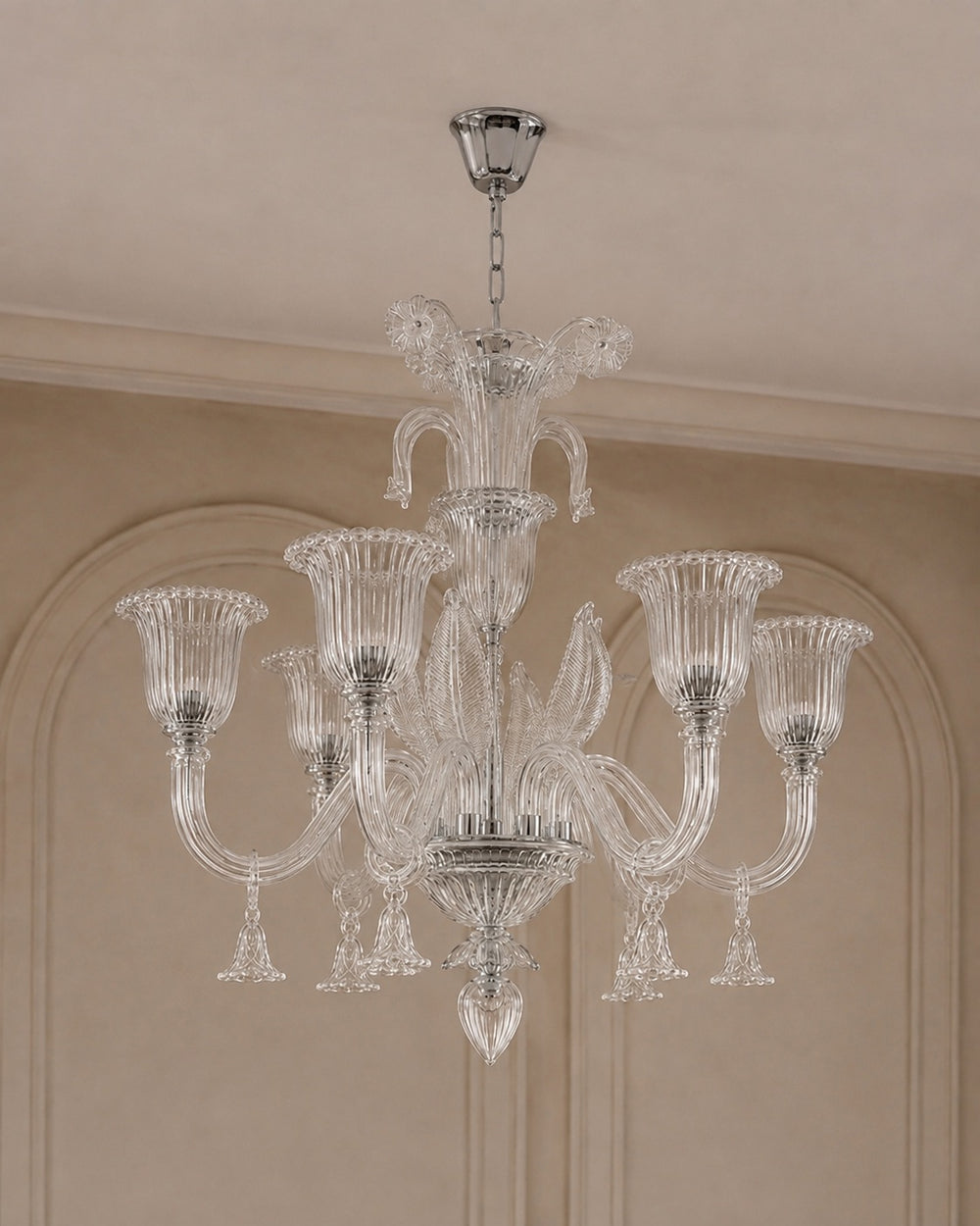 A multi-arm crystal chandelier with a polished silver-toned metal frame and clear glass shades, hanging from a ceiling in an elegant interior with beige walls and molding.