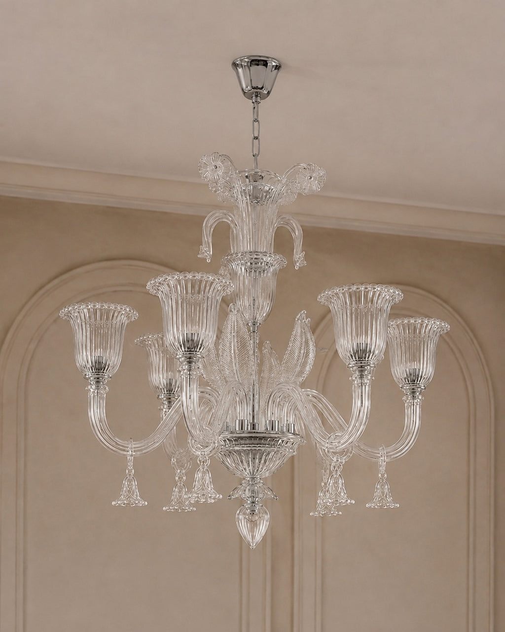 A multi-arm crystal chandelier with a polished silver-toned metal frame and clear glass shades, hanging from a ceiling in an elegant interior with beige walls and molding.