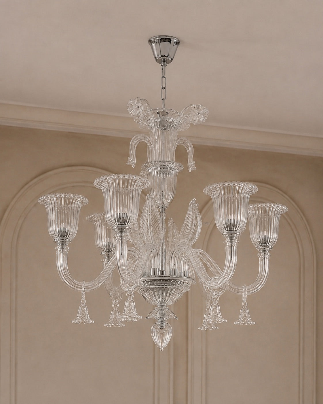 A multi-arm crystal chandelier with a polished silver-toned metal frame and clear glass shades, hanging from a ceiling in an elegant interior with beige walls and molding.