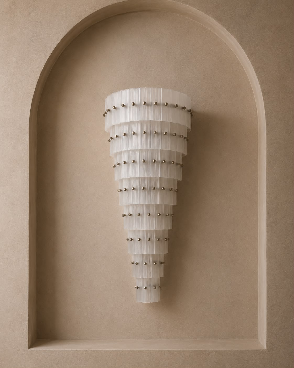 A modern tiered wall sconce with translucent white curved panels and small metallic studs, mounted on a beige plaster wall within an arched recess.