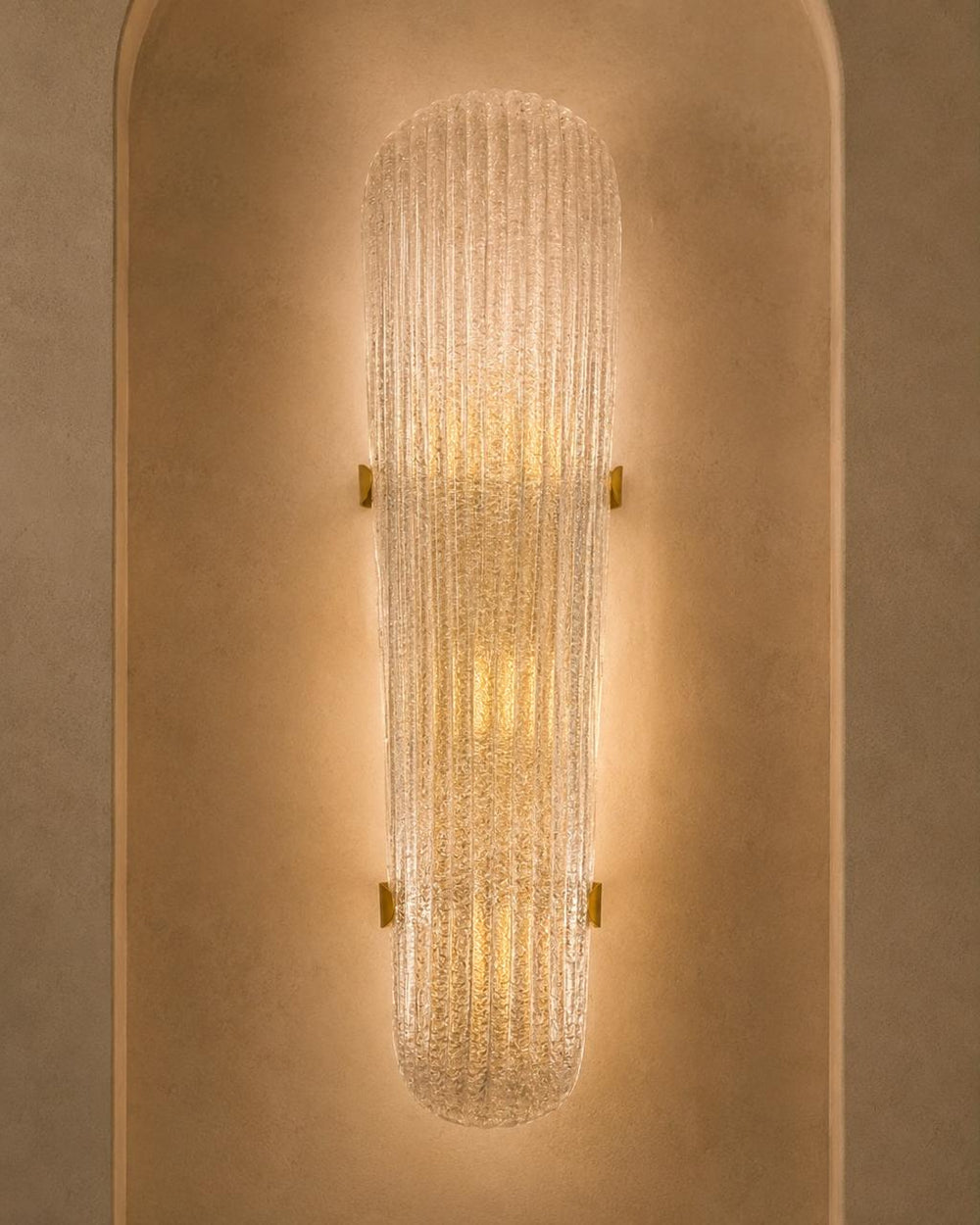 A modern wall sconce with a ribbed, textured glass shade that glows with warm light, mounted on a textured beige plaster wall.