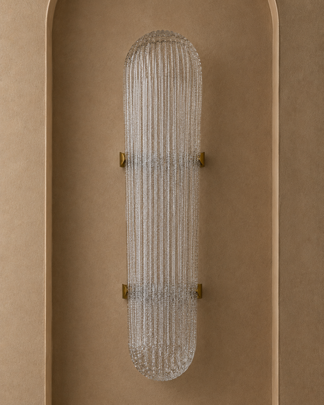 A modern wall-mounted light fixture with a ribbed clear glass shade and small gold metal brackets, centered against a warm beige textured wall.