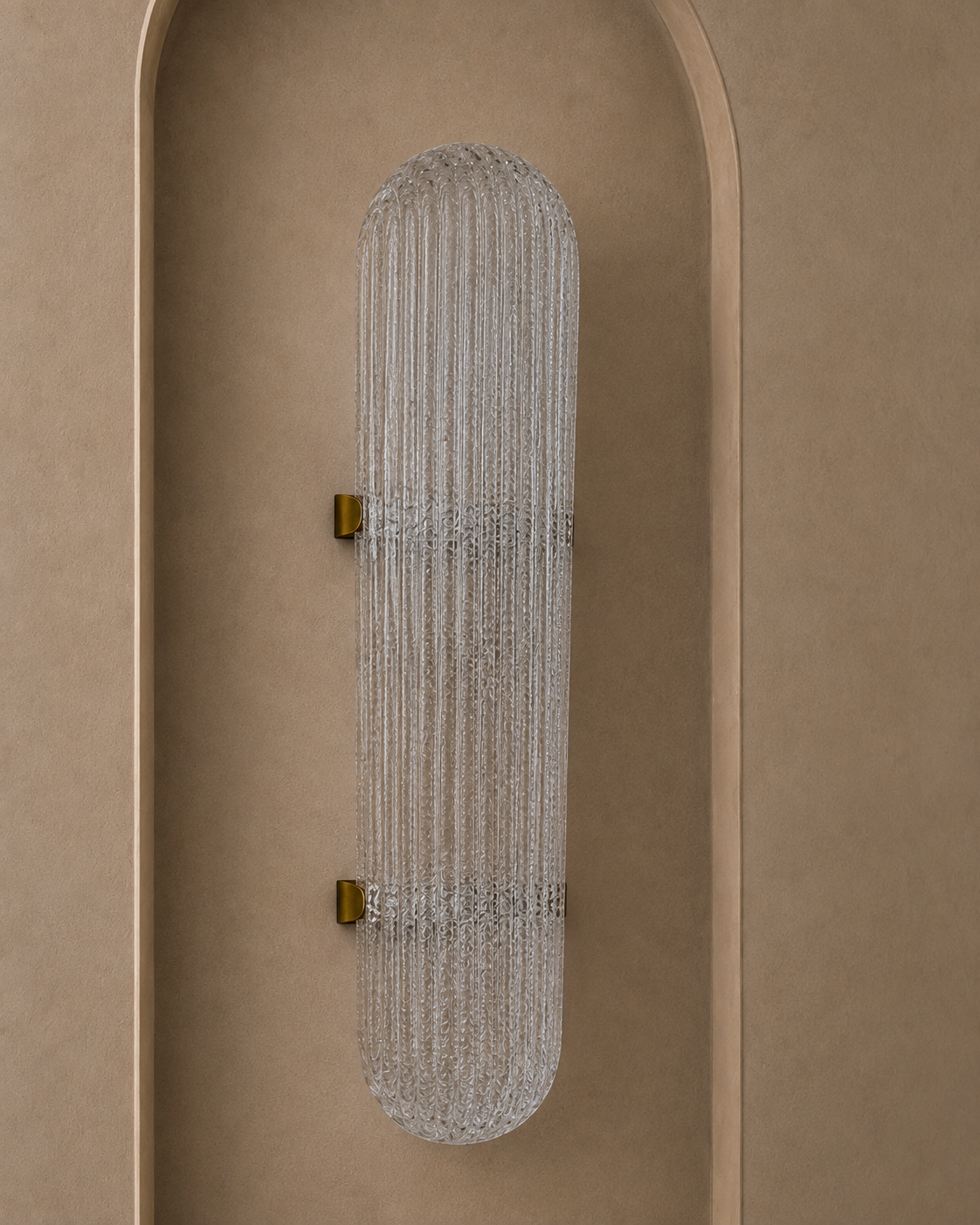 A modern wall sconce with a ribbed, vertically oriented cylindrical glass shade and small gold wall mounts, shown installed on a warm beige stucco wall with an arched recess.