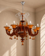 An ornate amber glass chandelier with six candle-style lights and clear crystal accents, hanging in a beige arched room.