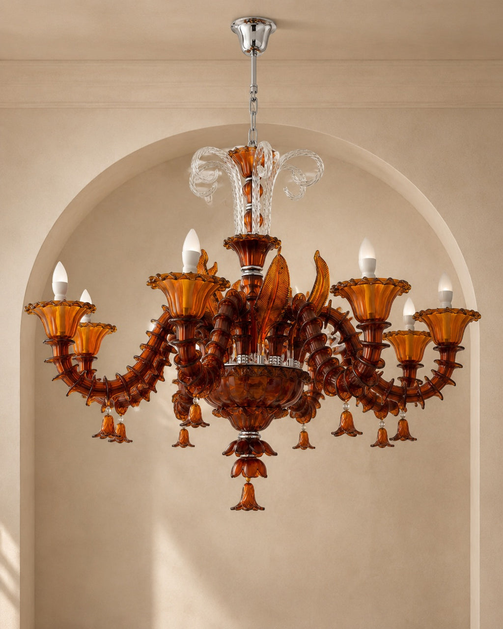 An ornate multi-arm chandelier made of amber-brown translucent glass with sculpted details, clear glass accents, and multiple candle-style bulbs, hanging in front of a beige arched wall.