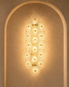 A modern wall sconce featuring multiple overlapping circular glass shades with gold-toned metal frames, mounted on a warm beige plaster wall within an arched niche.