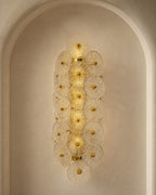 A vertical wall sconce with multiple overlapping circular glass shades and gold-toned metal accents, mounted in a tall arched alcove against a warm beige plaster wall.
