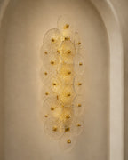 A modern wall sconce light fixture with multiple overlapping circular glass shades and gold-toned central bulbs, mounted on a beige plaster wall in an arched niche.